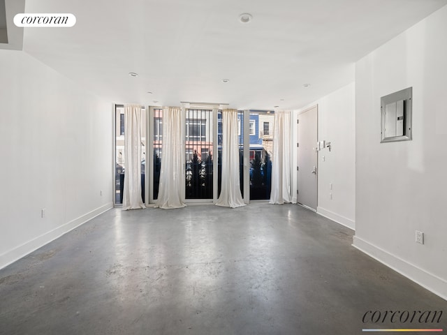 empty room with finished concrete flooring, visible vents, electric panel, and baseboards