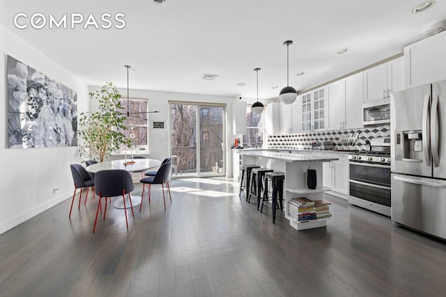 kitchen with dark wood-style floors, a breakfast bar area, stainless steel appliances, backsplash, and glass insert cabinets