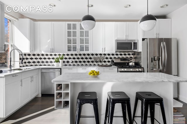 kitchen with a breakfast bar area, appliances with stainless steel finishes, white cabinetry, pendant lighting, and a sink