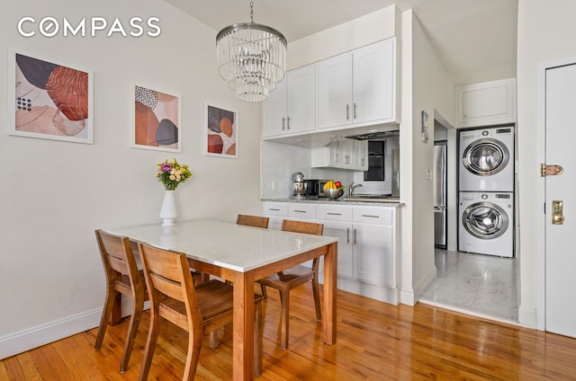 dining space with a notable chandelier, stacked washing maching and dryer, light wood-type flooring, and baseboards