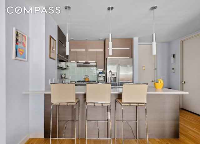 kitchen with tasteful backsplash, a breakfast bar area, high end refrigerator, a peninsula, and light wood-style floors