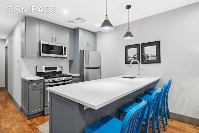 kitchen with gray cabinetry, light wood-style flooring, a kitchen breakfast bar, stainless steel appliances, and a sink