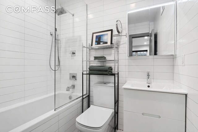 full bath featuring toilet, vanity, decorative backsplash, tiled shower / bath combo, and tile walls