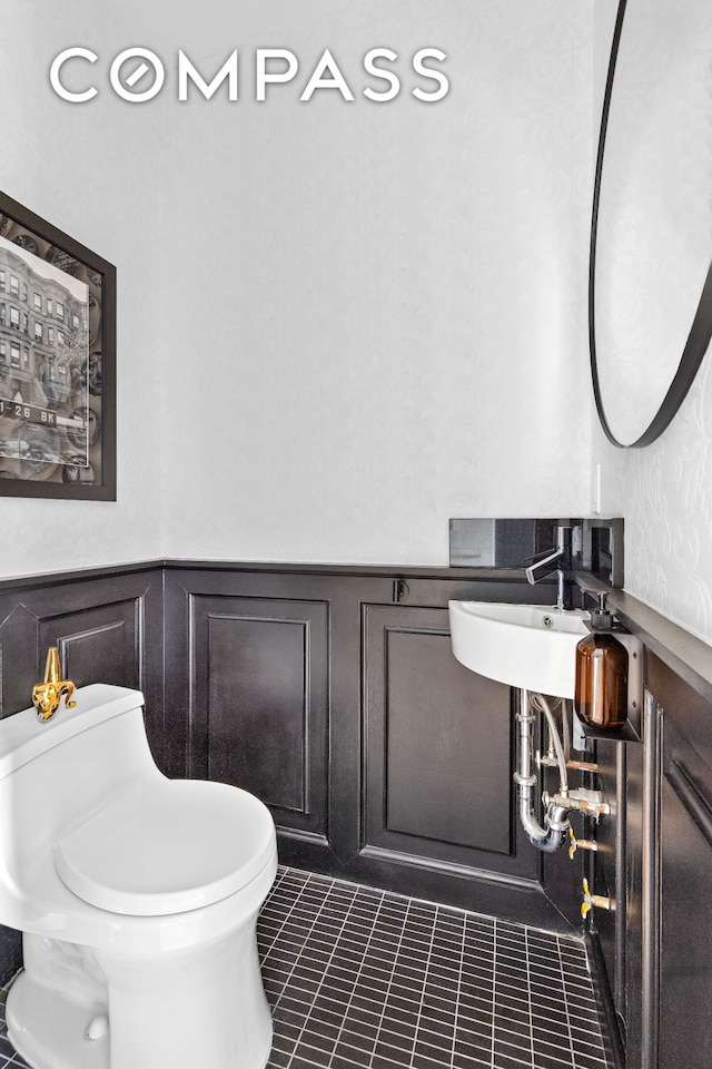 half bath featuring tile patterned floors, a wainscoted wall, toilet, and a decorative wall