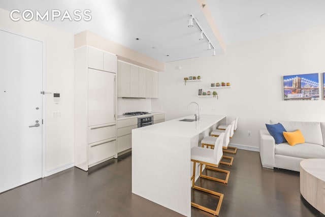 kitchen with a breakfast bar, a sink, light countertops, open shelves, and track lighting