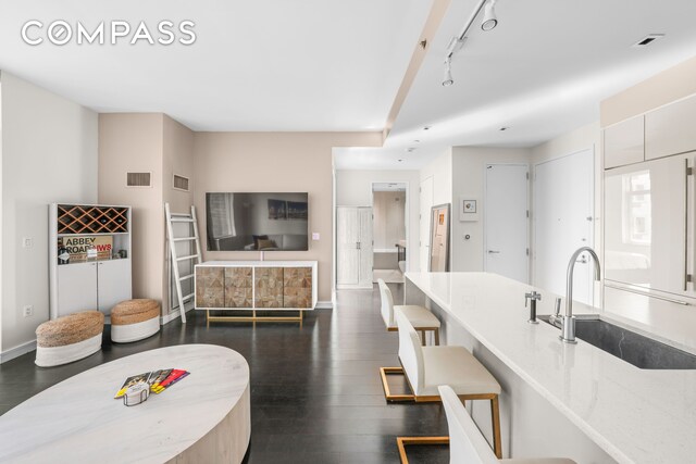 kitchen with baseboards, visible vents, a breakfast bar area, dark wood-type flooring, and a sink