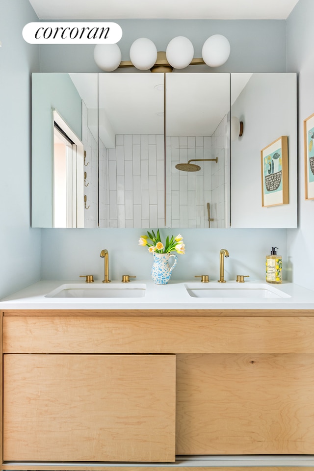 bathroom with tiled shower, a sink, and double vanity