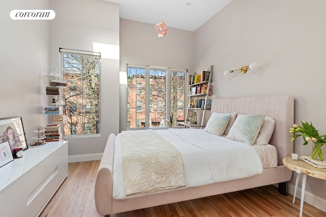 bedroom with light wood-style floors, a towering ceiling, and baseboards