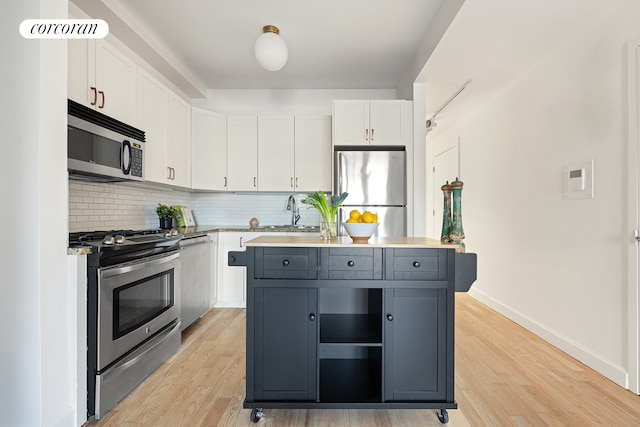 kitchen with backsplash, appliances with stainless steel finishes, white cabinets, a kitchen island, and a sink