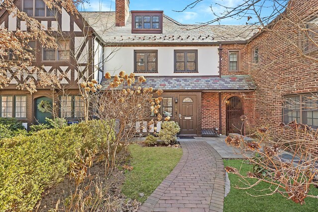 view of front of home with a high end roof, brick siding, a chimney, and stucco siding