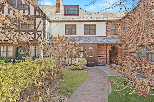 view of front facade with brick siding, a high end roof, stucco siding, and a chimney