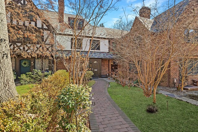 tudor house featuring a high end roof, brick siding, a chimney, and a front yard