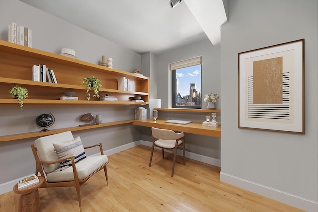 office space featuring light wood-style flooring, built in desk, and baseboards