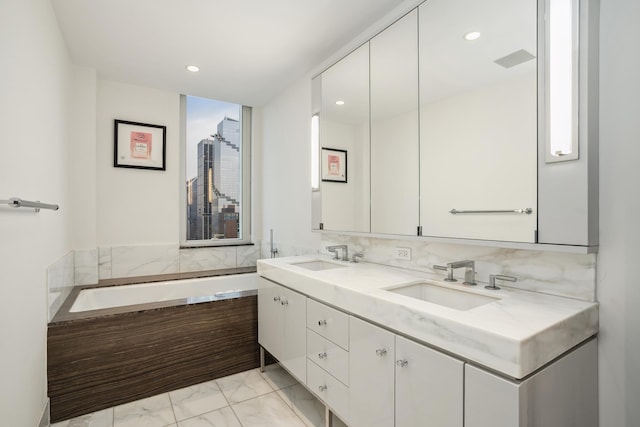 full bathroom featuring double vanity, marble finish floor, a garden tub, and a sink