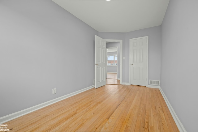 unfurnished room with wood-type flooring, visible vents, and baseboards