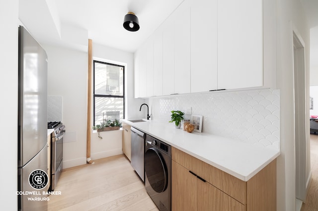 kitchen with a sink, backsplash, washer / dryer, stainless steel appliances, and modern cabinets