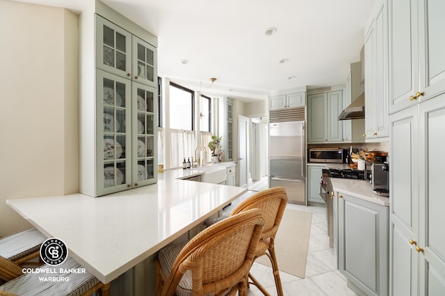 kitchen with light tile patterned floors, high quality appliances, a breakfast bar area, glass insert cabinets, and a peninsula