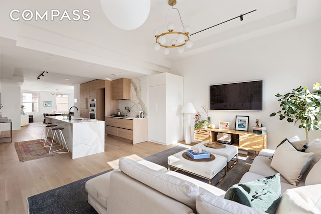 living area with a tray ceiling, light wood-style floors, and an inviting chandelier