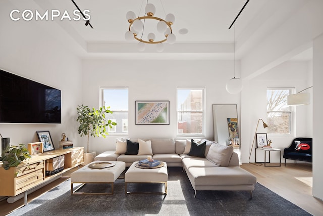 living area featuring a chandelier, a raised ceiling, and wood finished floors