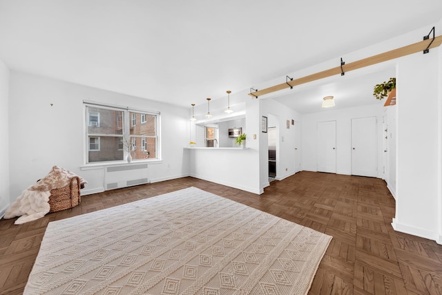unfurnished living room with radiator heating unit, a barn door, and baseboards