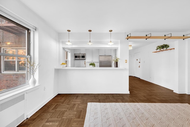 kitchen with stainless steel appliances, baseboards, light countertops, radiator, and decorative light fixtures