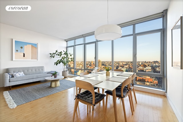 dining area with floor to ceiling windows, a city view, visible vents, light wood-type flooring, and baseboards