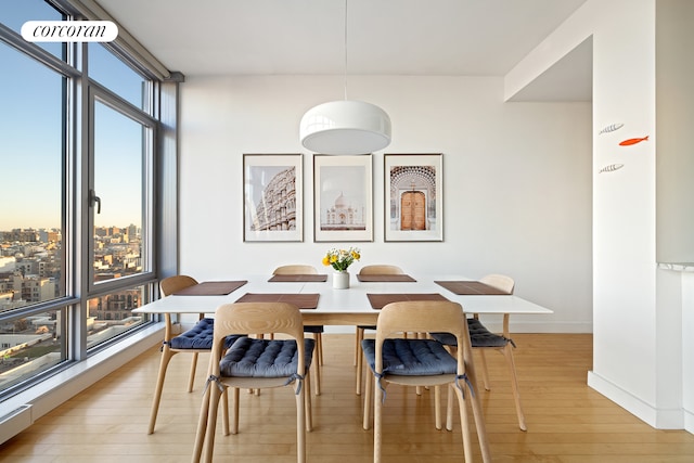 dining space featuring light wood-style floors, baseboards, and a wall of windows