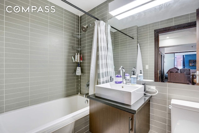 full bathroom featuring tiled shower / bath combo, toilet, tile walls, and vanity