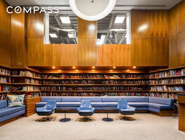 living area featuring wall of books, carpet floors, and wooden walls