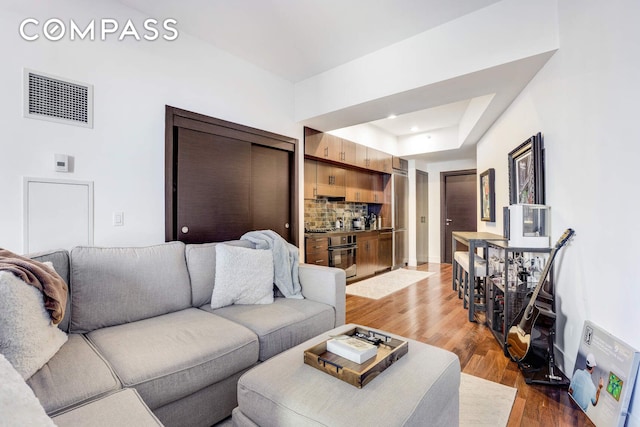 living area with recessed lighting, visible vents, wood finished floors, and a raised ceiling