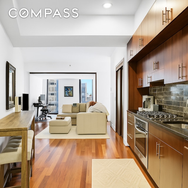 kitchen featuring backsplash, light wood finished floors, open floor plan, and oven