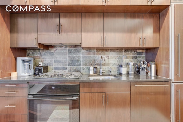 kitchen featuring a sink, decorative backsplash, black oven, and stainless steel gas stovetop