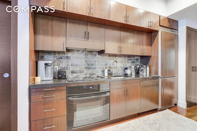 kitchen with decorative backsplash, wood finished floors, a sink, stainless steel gas stovetop, and oven