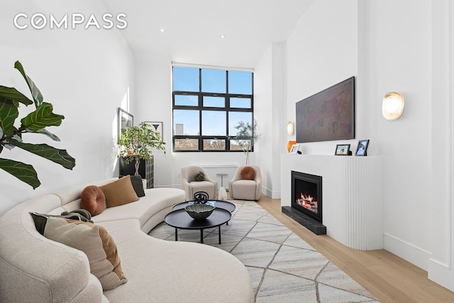 living area featuring baseboards, a lit fireplace, a towering ceiling, and wood finished floors