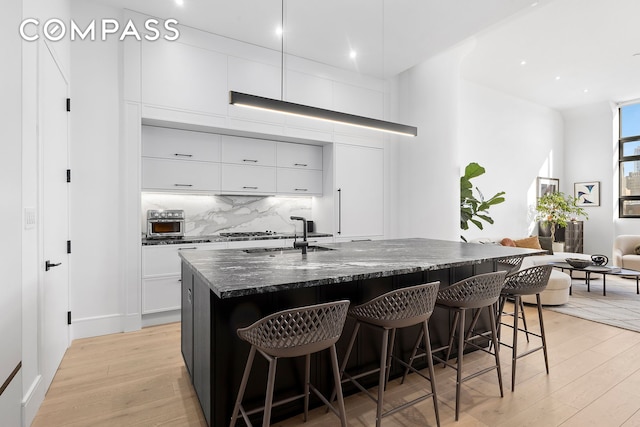 kitchen with a breakfast bar, a sink, backsplash, and light wood finished floors