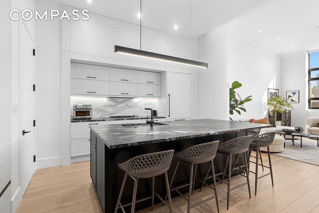 kitchen with a sink, decorative backsplash, light wood-style floors, and a breakfast bar