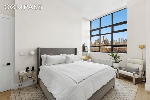 bedroom featuring light wood-type flooring, a city view, and baseboards