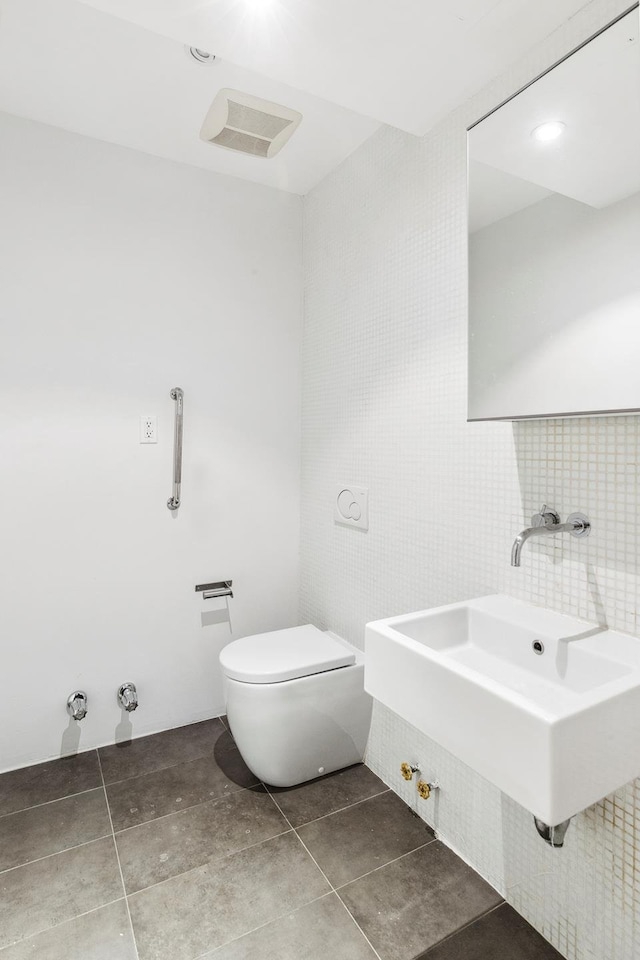 half bathroom featuring toilet, tile walls, a sink, tile patterned floors, and backsplash