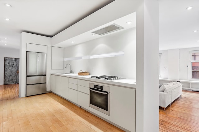 kitchen with appliances with stainless steel finishes, modern cabinets, white cabinets, light wood finished floors, and recessed lighting