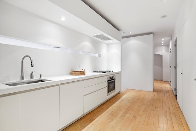kitchen with a sink, stainless steel oven, light wood-style flooring, white cabinets, and recessed lighting