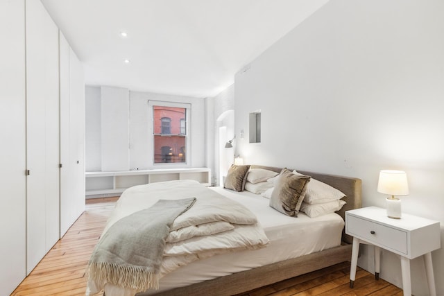 bedroom with light wood-style flooring, arched walkways, and recessed lighting