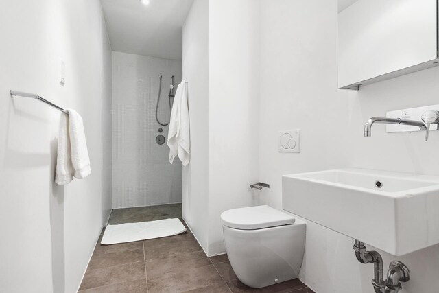 full bathroom with a sink, tile patterned flooring, a tile shower, and toilet