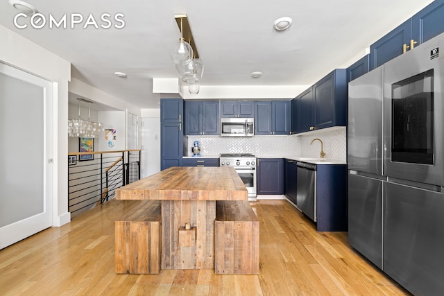 kitchen with stainless steel appliances, blue cabinets, light wood-style floors, and backsplash