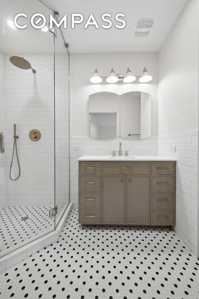 full bath with a wainscoted wall, tile walls, visible vents, a stall shower, and vanity