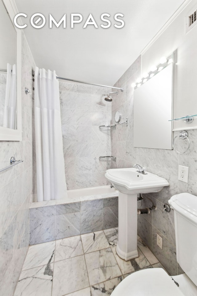 full bathroom featuring toilet, tiled shower / bath, visible vents, and tile walls