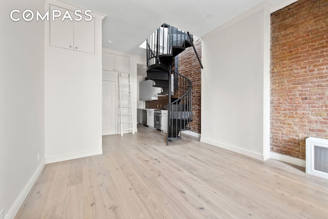 interior space featuring light wood finished floors, visible vents, brick wall, baseboards, and stairs