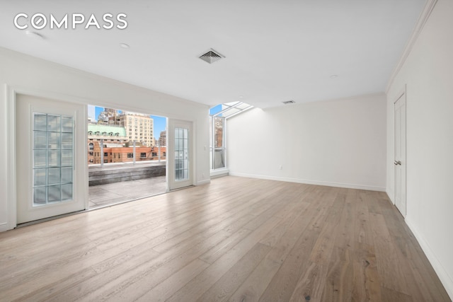 unfurnished living room featuring a city view, visible vents, ornamental molding, wood finished floors, and baseboards