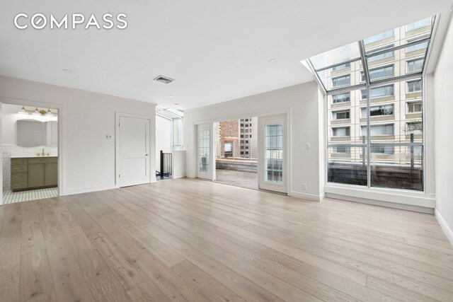 unfurnished living room with a skylight, visible vents, baseboards, light wood-style floors, and a sink