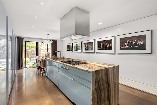 kitchen with concrete floors, a sink, wall chimney range hood, stainless steel gas stovetop, and light stone counters