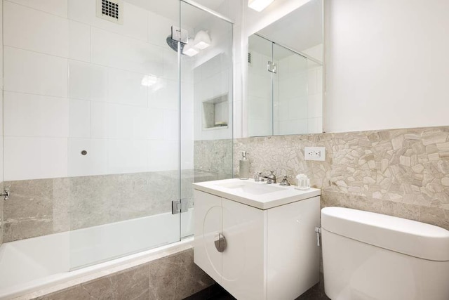 bathroom with visible vents, tiled shower, toilet, vanity, and tile walls